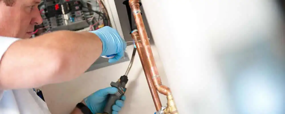Water heater repair technician testing copper pipe connections and controls in Arlington, TX